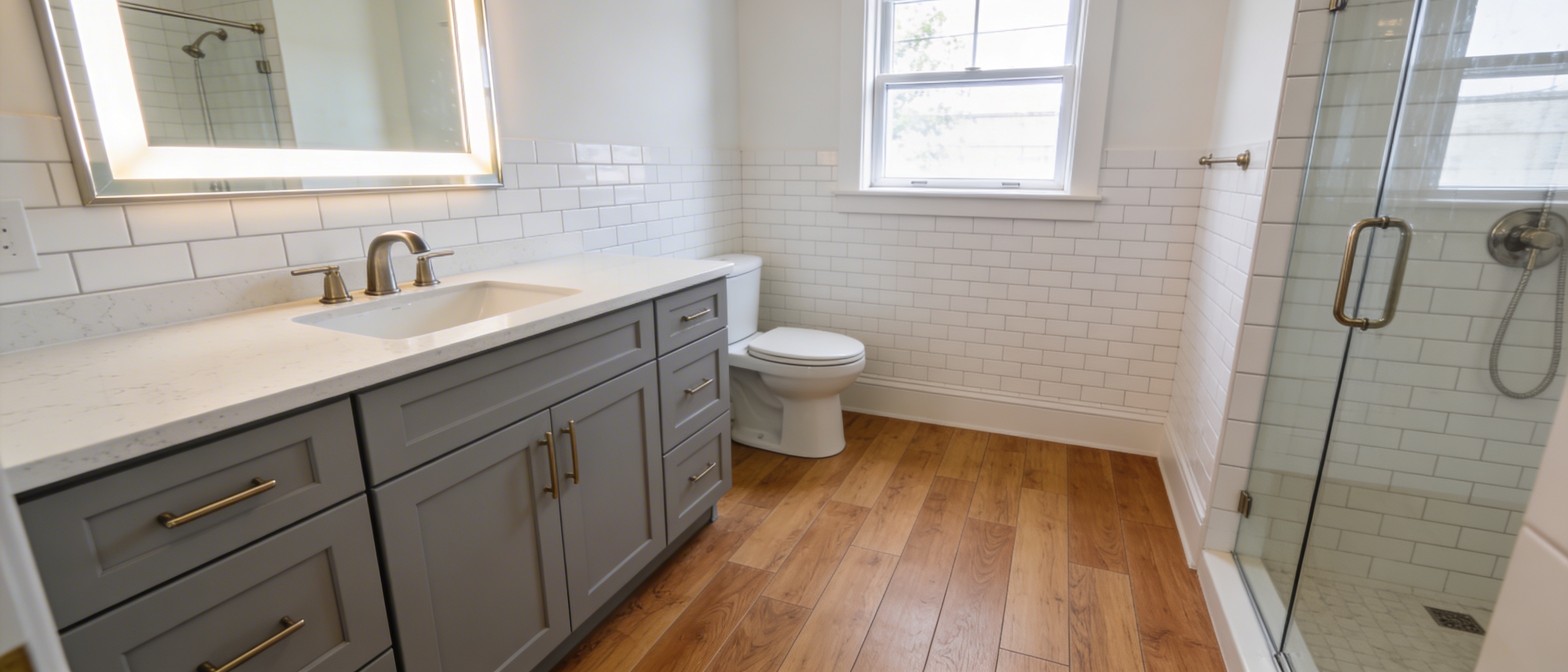 Renovated apartment bathroom with oak-toned flooring, grey vanity, toilet, and window above the toilet.